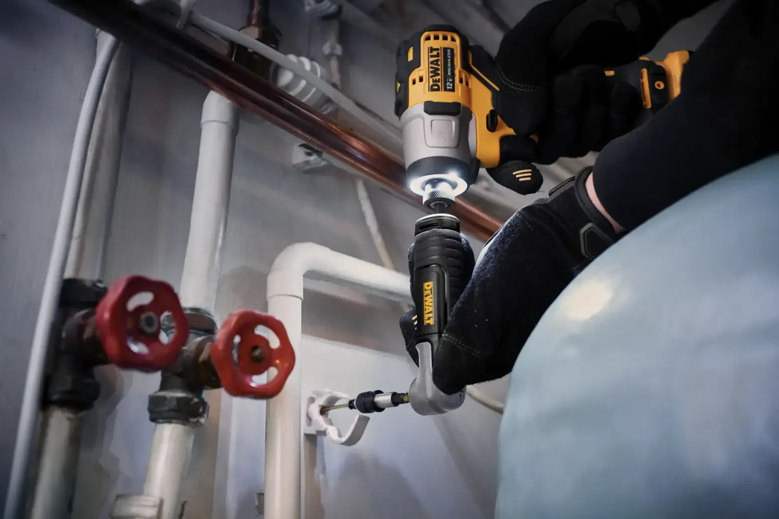 Operario con un atornillador de impacto DEWALT y un accesorio flexible en ángulo junto a tuberías